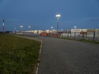 an empty street with traffic lights in the distance and large containers behind it at night