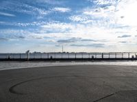 a person in yellow shirt flying a kite over a cement parking lot by water and a pier