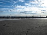 a person in yellow shirt flying a kite over a cement parking lot by water and a pier