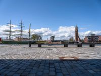 a large ship is in the harbor with buildings behind it and a bench at the front