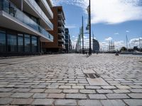 a cobbled sidewalk in a public setting with some tall buildings near by and a blue sky