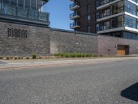 a view of a city street in front of an apartment building with a brick wall