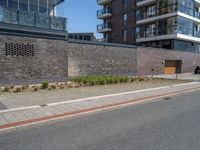 a view of a city street in front of an apartment building with a brick wall