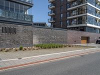 a view of a city street in front of an apartment building with a brick wall