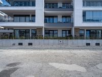 a big white building near a dirt lot next to a street corner with bushes in front of it