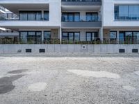 a big white building near a dirt lot next to a street corner with bushes in front of it