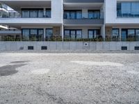 a big white building near a dirt lot next to a street corner with bushes in front of it