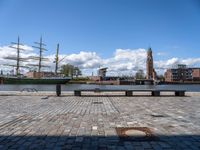 a square with benches and a sailboat in the background, in front of a brick walkway with cobblestones on it