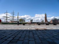 a square with benches and a sailboat in the background, in front of a brick walkway with cobblestones on it