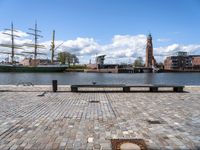 a square with benches and a sailboat in the background, in front of a brick walkway with cobblestones on it