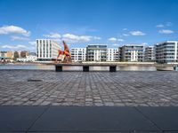 a park bench sitting on the edge of a dock with buildings behind it and blue skies