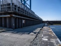 an empty road near the water and an overpass for a bike path with people walking down it