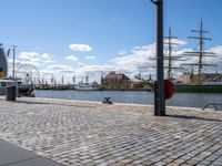 the cobble - stone path of the docks is lined with tall masts, large sails and bright blue skies