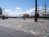 the cobble - stone path of the docks is lined with tall masts, large sails and bright blue skies