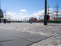 the cobble - stone path of the docks is lined with tall masts, large sails and bright blue skies