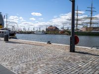 the cobble - stone path of the docks is lined with tall masts, large sails and bright blue skies