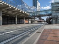 a bus driving past a long bridge over a street underneath a tall building with glass doors