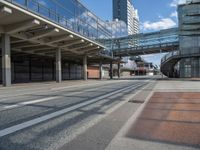 a bus driving past a long bridge over a street underneath a tall building with glass doors