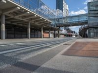 a bus driving past a long bridge over a street underneath a tall building with glass doors