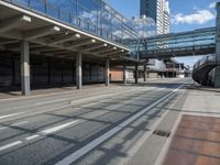 a bus driving past a long bridge over a street underneath a tall building with glass doors