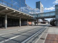 a bus driving past a long bridge over a street underneath a tall building with glass doors