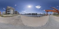 a fisheye lens on a bike trail next to a lake and buildings with a bright sun