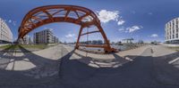 an upside down panorama with an open orange structure near buildings and a walkway next to the water