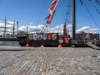 a boat docked on a brick walkway with a flag and flag poles in the background