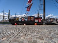 a boat docked on a brick walkway with a flag and flag poles in the background