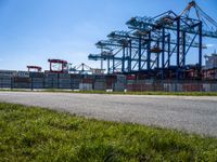 a road running through the grass near a construction crane in an industrial area with green grass