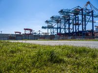 a road running through the grass near a construction crane in an industrial area with green grass