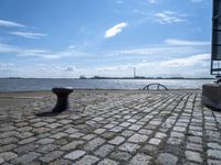 a large bricked area next to a body of water with a bench by it