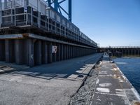 a man rides a bike down a concrete path by the water's edge with steel railings that protect traffic on it