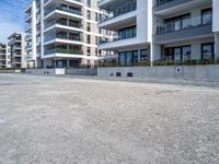 an empty parking lot in front of high rise apartments or apartment complexes, with no sidewalks or trees on the ground