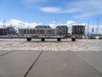 a stone bench on the ground near a body of water with buildings in the background