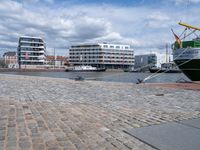 the large boat is docked on the harbor shore of a city near many buildings with windows