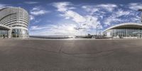 a fisheye view of two buildings in front of the ocean with a blue sky and a few clouds