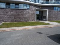 a building with grass next to it on a street corner with cars parked at the curb