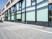 glass - trimmed building with modern parking in front of it on a sidewalk beside a pedestrian