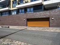 a sidewalk near some cars and a brick building with a orange garage door on the side of it