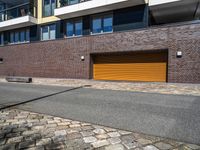 a sidewalk near some cars and a brick building with a orange garage door on the side of it