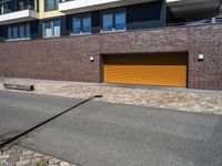 a sidewalk near some cars and a brick building with a orange garage door on the side of it