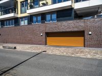 a sidewalk near some cars and a brick building with a orange garage door on the side of it