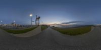 two street lamps on a long paved pathway with a lighthouse in the background at dusk