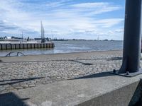 an empty concrete bench near some water and buildings in the background of a stone walkway