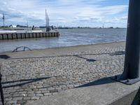 an empty concrete bench near some water and buildings in the background of a stone walkway