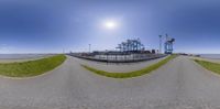 a street, fence and grass are seen in this fish eye view lens photograph taken from a fish hole