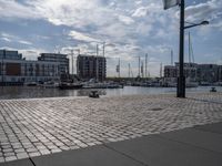 the pavement has stone pavers on it and boats are parked outside in the harbor