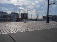 the pavement has stone pavers on it and boats are parked outside in the harbor