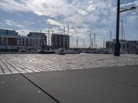 the pavement has stone pavers on it and boats are parked outside in the harbor